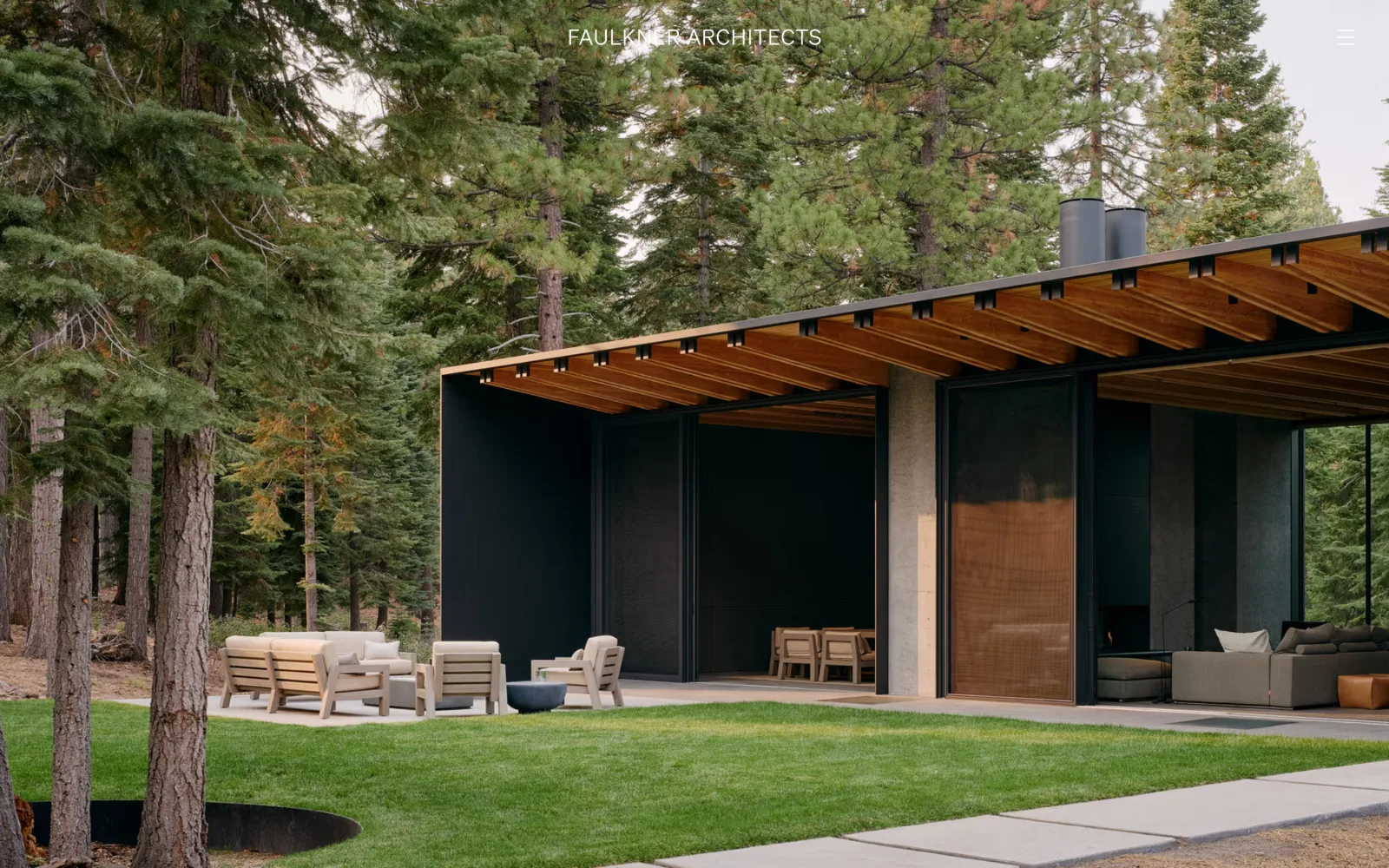 faulknerarchitects.com, architect website design: a low house with a deep timber eave sits among tall pines on cut grass, filling the frame