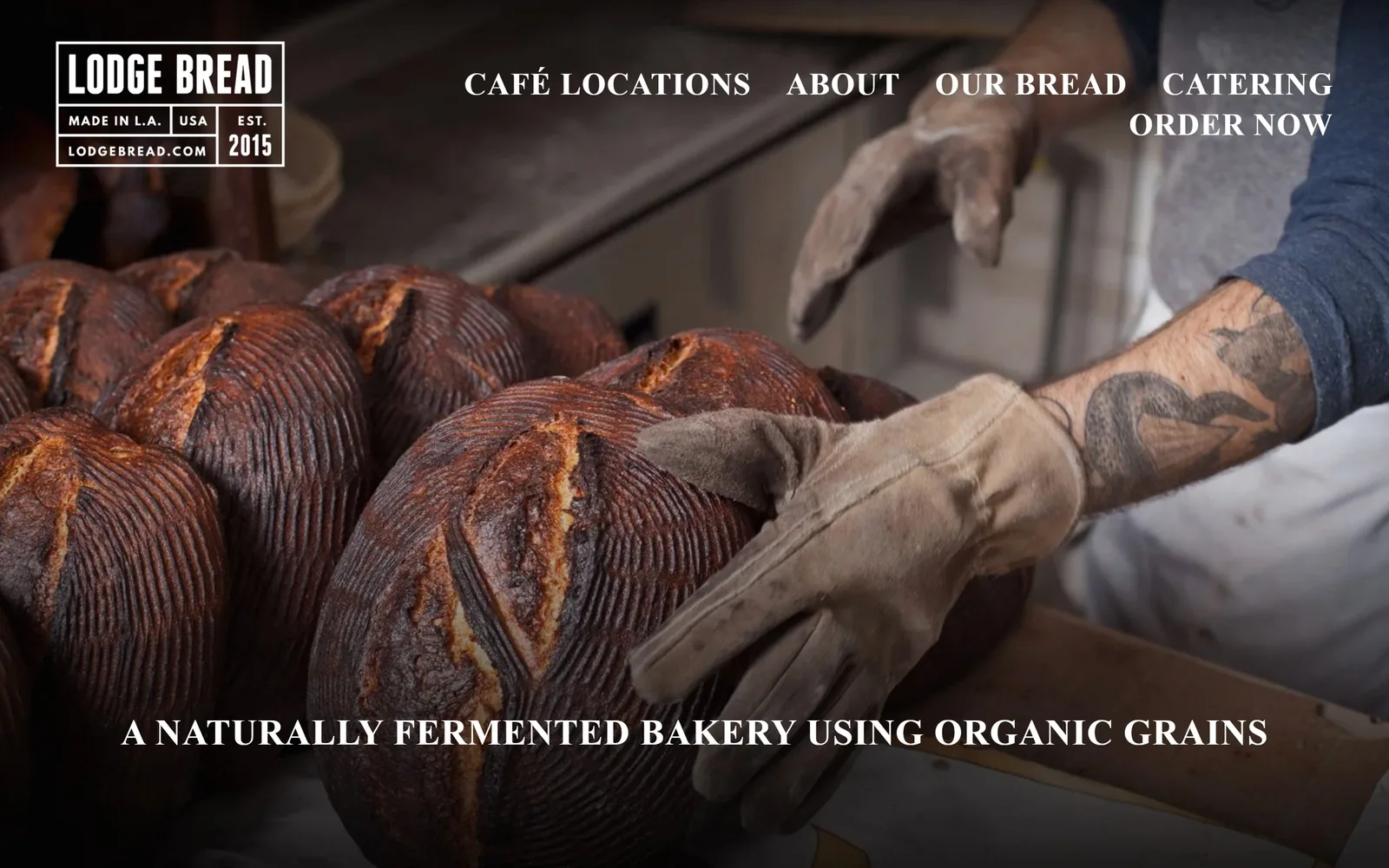 lodgebread.com, bakery website design: a baker in a welding glove turning scored sourdough in low light