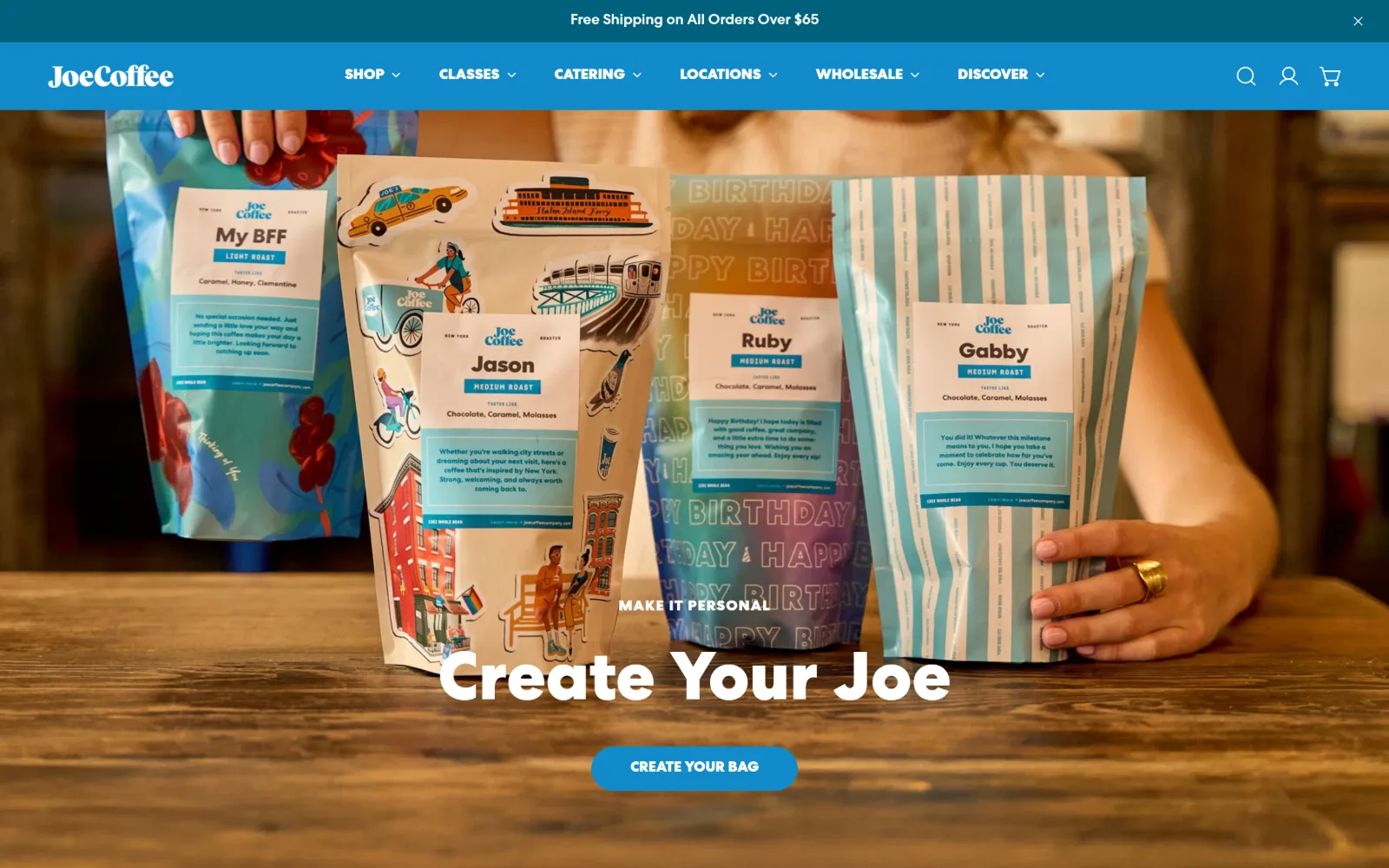 joecoffeecompany.com, coffee shop website design: four illustrated coffee bags are held across a wooden counter under a white Create Your