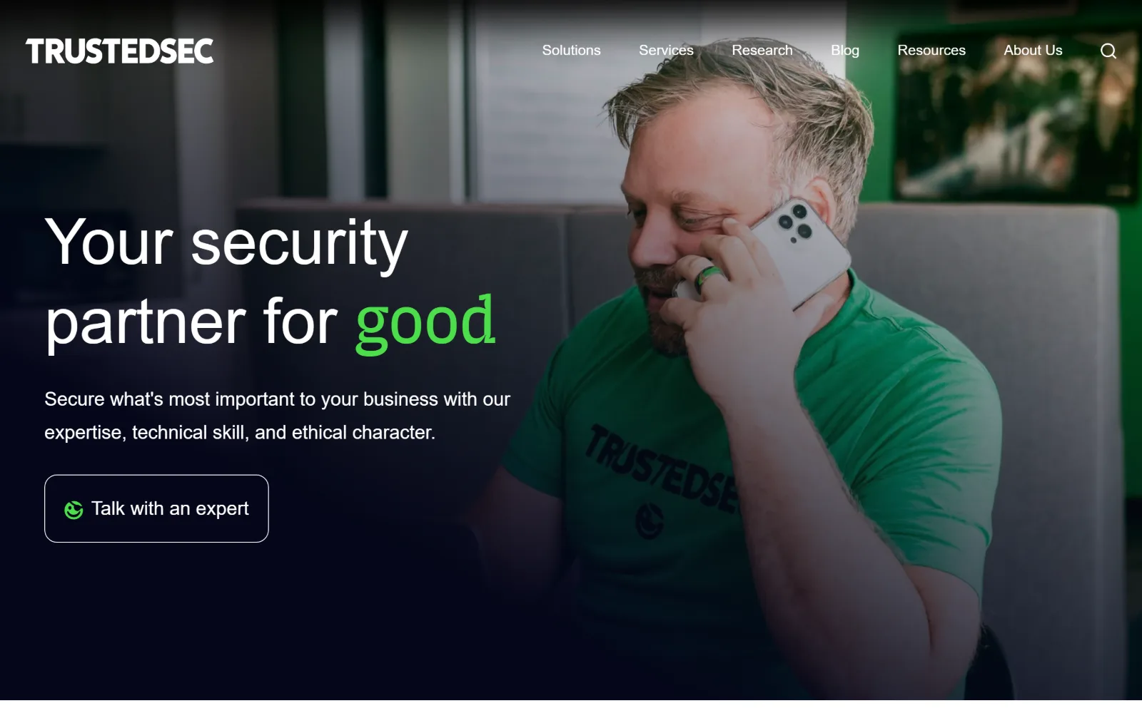 trustedsec.com, cyber security website design: a full-bleed photo of a man in a green branded t-shirt on the phone