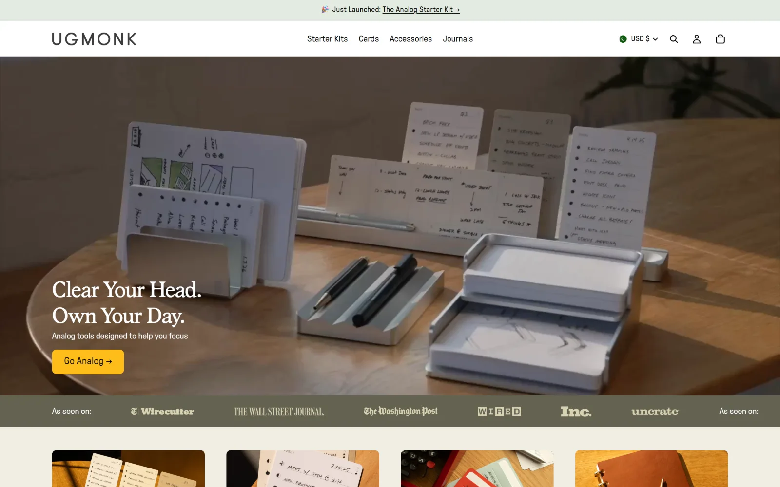 ugmonk.com, ecommerce website design: desk cards and aluminium trays fill a video hero behind a two line serif headline and a single