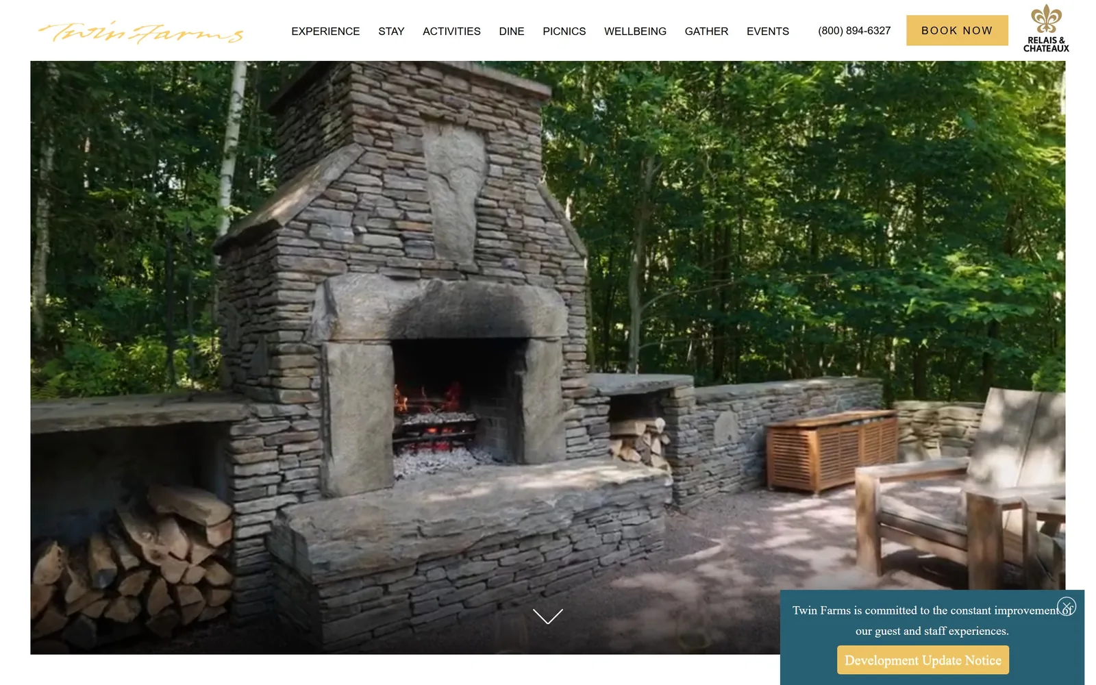 twinfarms.com, hotel website design: an outdoor dry-stone fireplace with a live fire and split logs stacked beside it