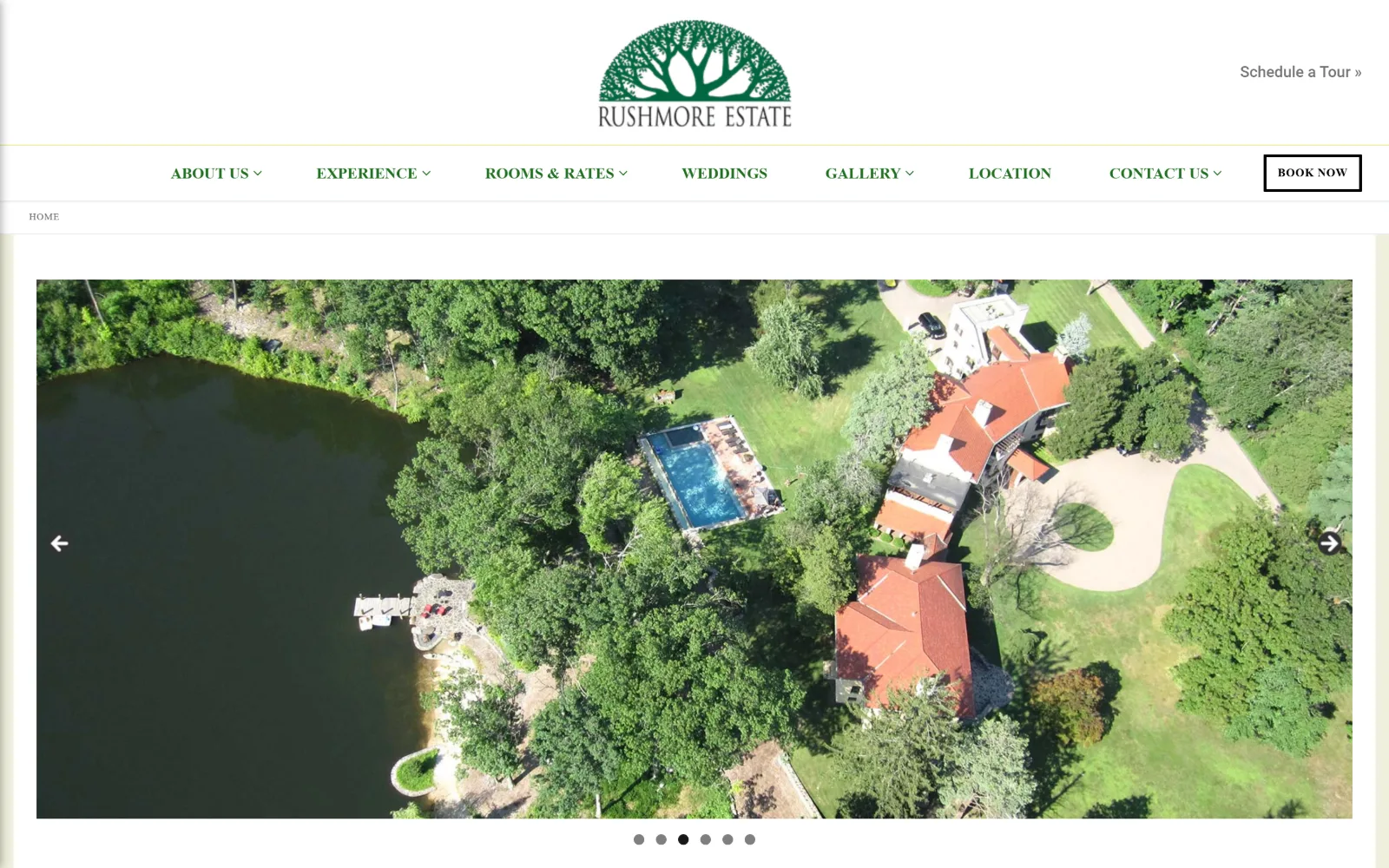 rushmoreestate.com, wedding venue website design: six slider dots sit under a contained aerial of a tiled-roof estate beside a lake